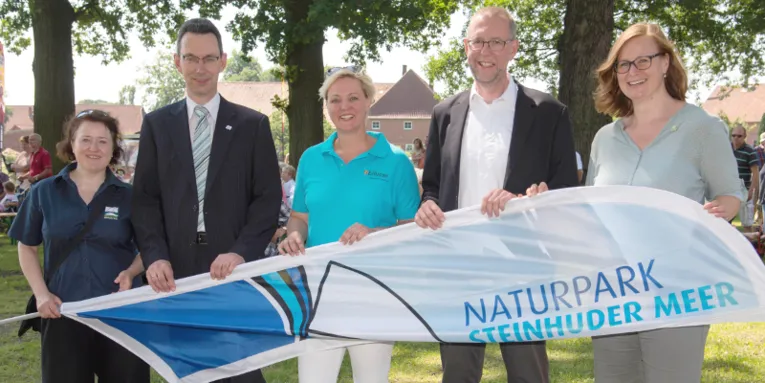 Drei Frauen und zwei Männer stehen nebeneinander und halten gemeinsam eine Strandflagge.