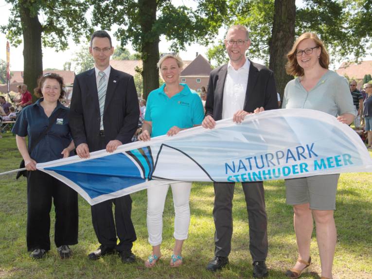 Drei Frauen und zwei Männer stehen nebeneinander und halten gemeinsam eine Strandflagge.