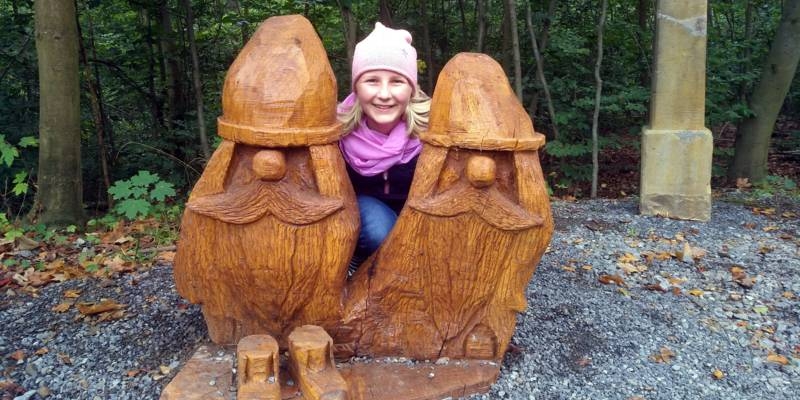 Ein Kind steht zwischen zwei aus Holz geschnitzten Wichtelmännchen.