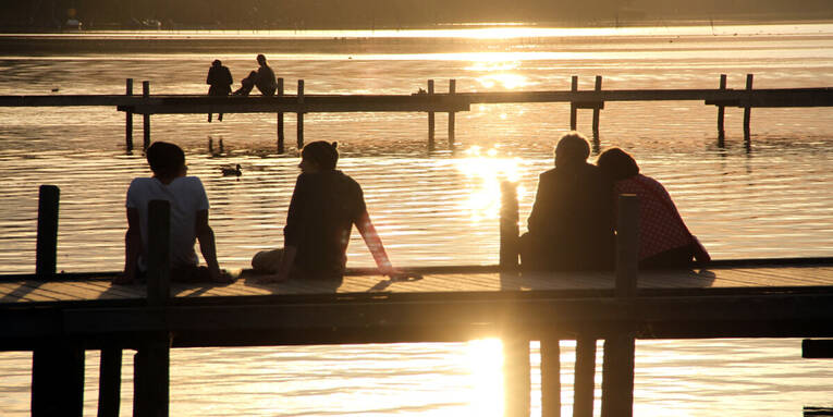 Zwei Steege ragen ins Steinhuder Meer, darauf sitzen sechs Menschen während die Sonne untergeht. Zwei Steege ragen ins Steinhuder Meer, darauf sitzen sechs Menschen während die Sonne untergeht.