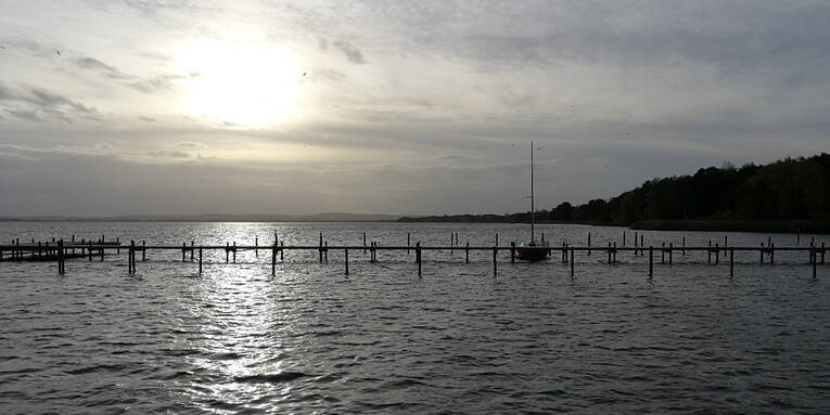 Über einem Steg am Steinhuder Meer geht die Sonne unter. An dem Steg ist ein einzelnes Boot vertäut. Über einem Steg am Steinhuder Meer geht die Sonne unter. An dem Steg ist ein einzelnes Boot vertäut.