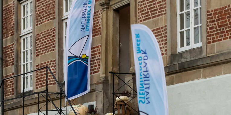 Zwei Beachflags mit dem Logo des Naturparks Steinhuder stehen auf einer Treppe zu einem Eingang von Schloss Landestrost in Neustadt am Rübenberge. Zwei Beachflags mit dem Logo des Naturparks Steinhuder stehen auf einer Treppe zu einem Eingang von Schloss Landestrost in Neustadt am Rübenberge.