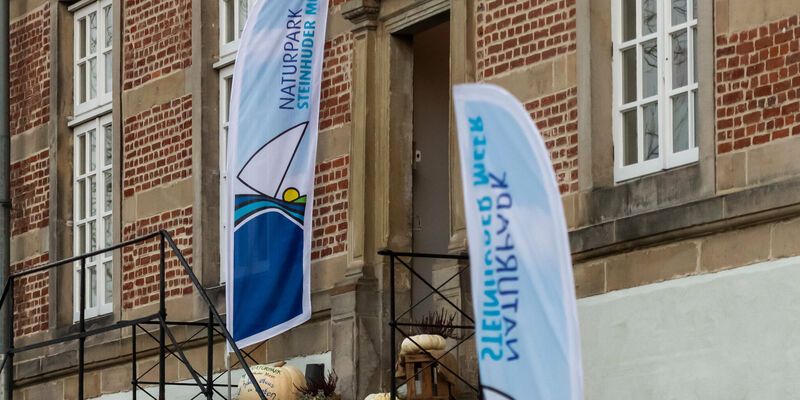 Zwei Beachflags mit dem Logo des Naturparks Steinhuder stehen auf einer Treppe zu einem Eingang von Schloss Landestrost in Neustadt am Rübenberge. Zwei Beachflags mit dem Logo des Naturparks Steinhuder stehen auf einer Treppe zu einem Eingang von Schloss Landestrost in Neustadt am Rübenberge.