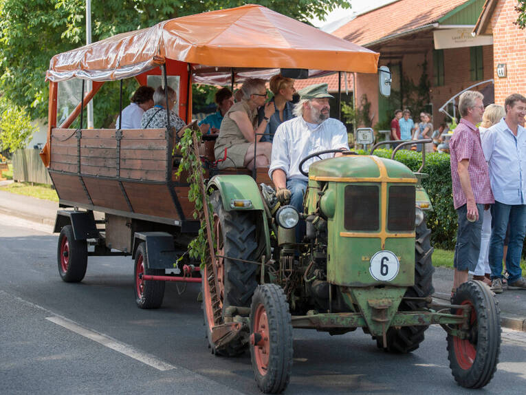Ein Oldtimer-Trecker zieht einen Planwagen, darauf fahren Menschen mit. Ein Oldtimer-Trecker zieht einen Planwagen, darauf fahren Menschen mit.