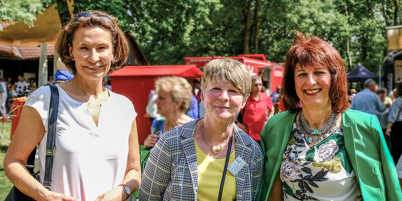 Drei Frauen stehen nebeneinander, dahinter wird ein Fest gefeiert. Drei Frauen stehen nebeneinander, dahinter wird ein Fest gefeiert.